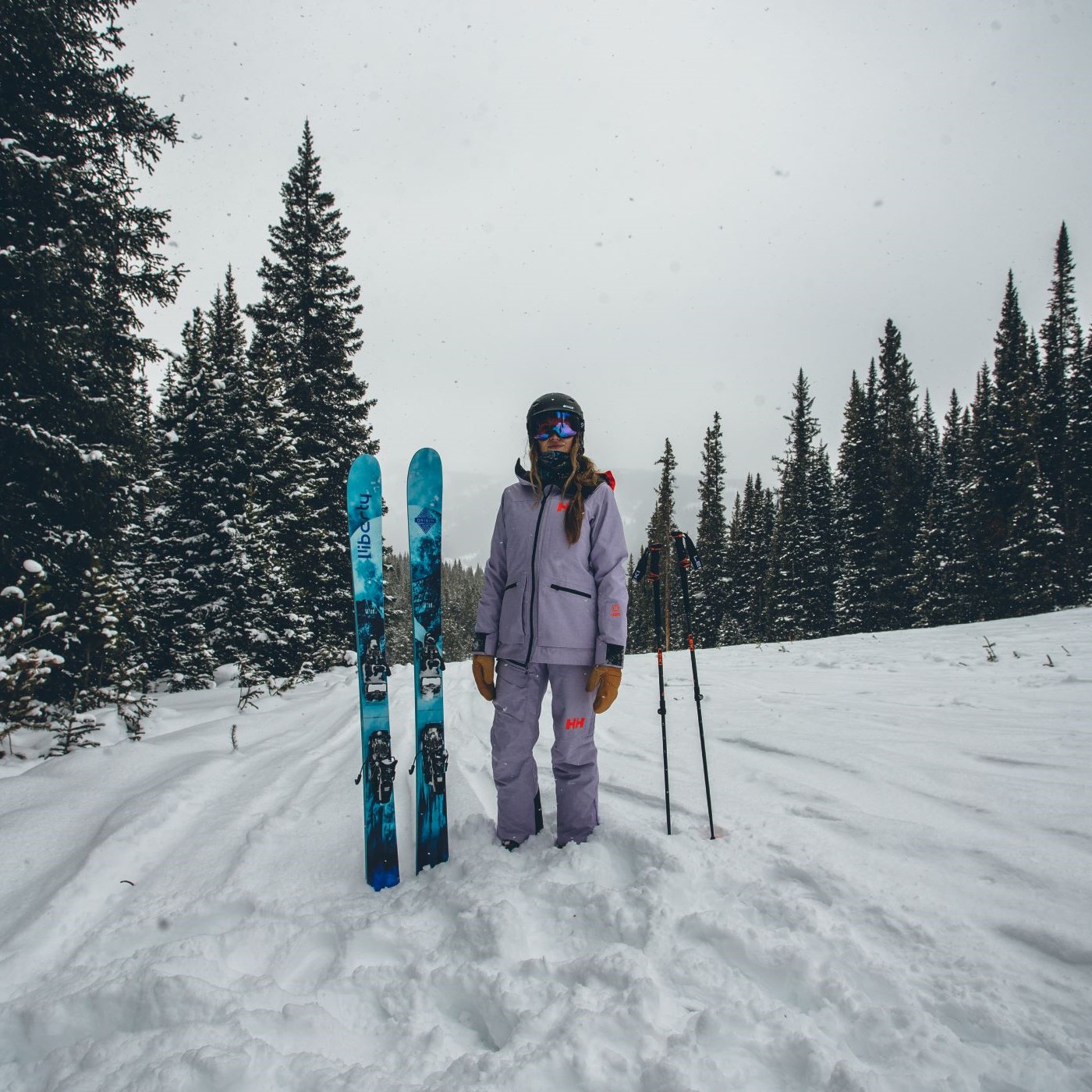 A woman on top of a mountain with skis and a ski jacket and pants. 