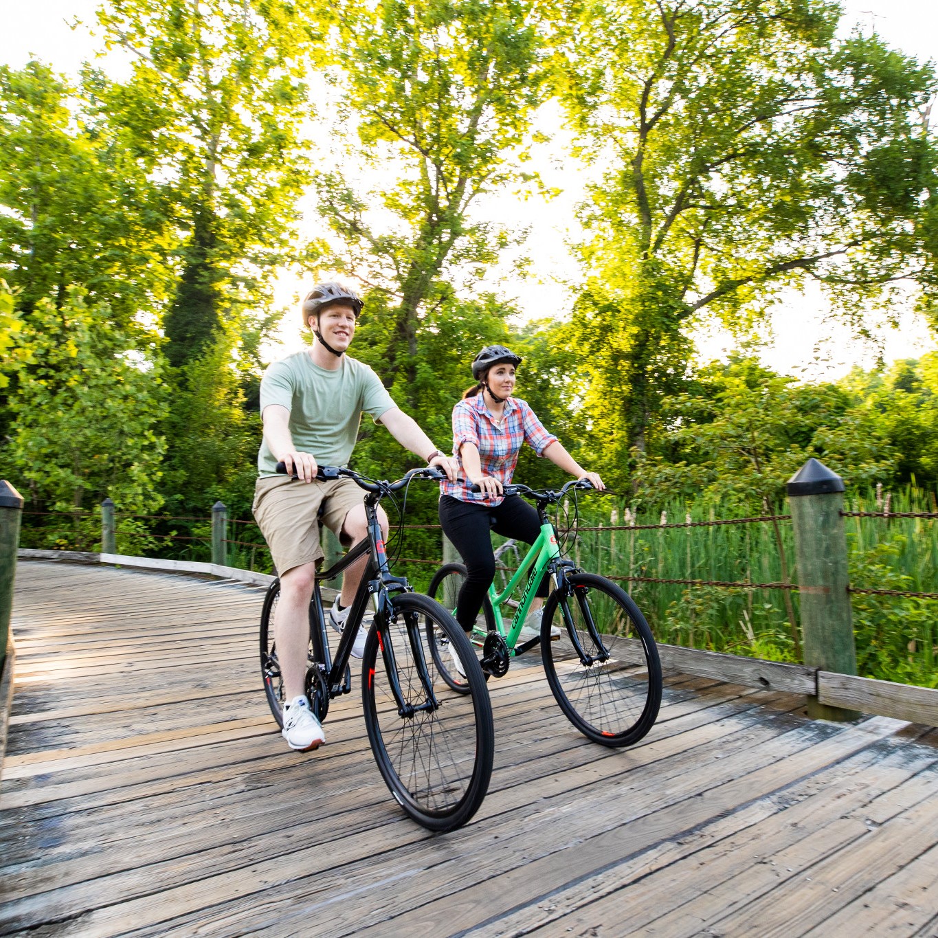 man and woman riding a bike priced under $1,000.00 over a wooden bridge in a park.
