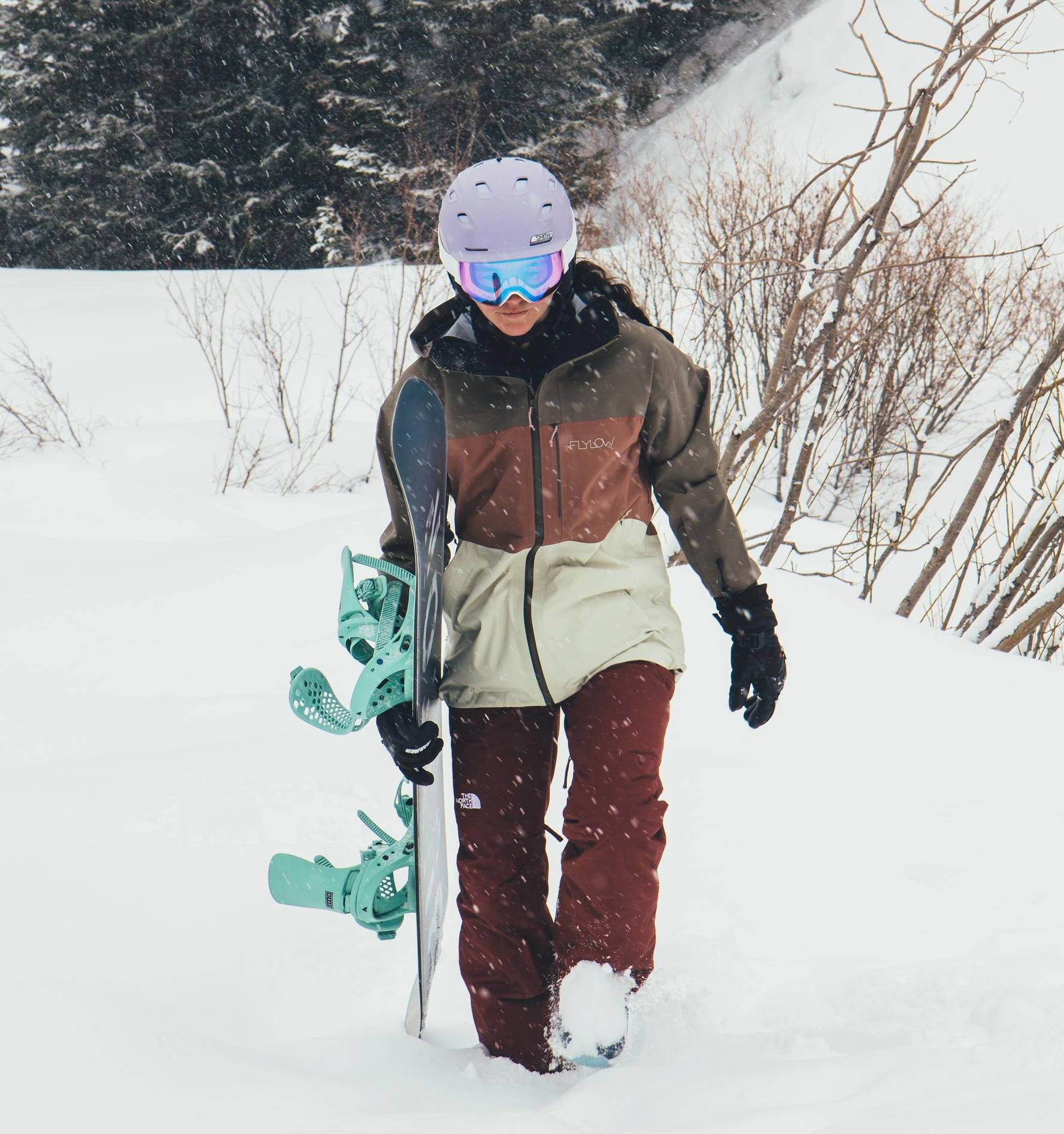 Snowboarder walking through deep snow while carrying a snowboard