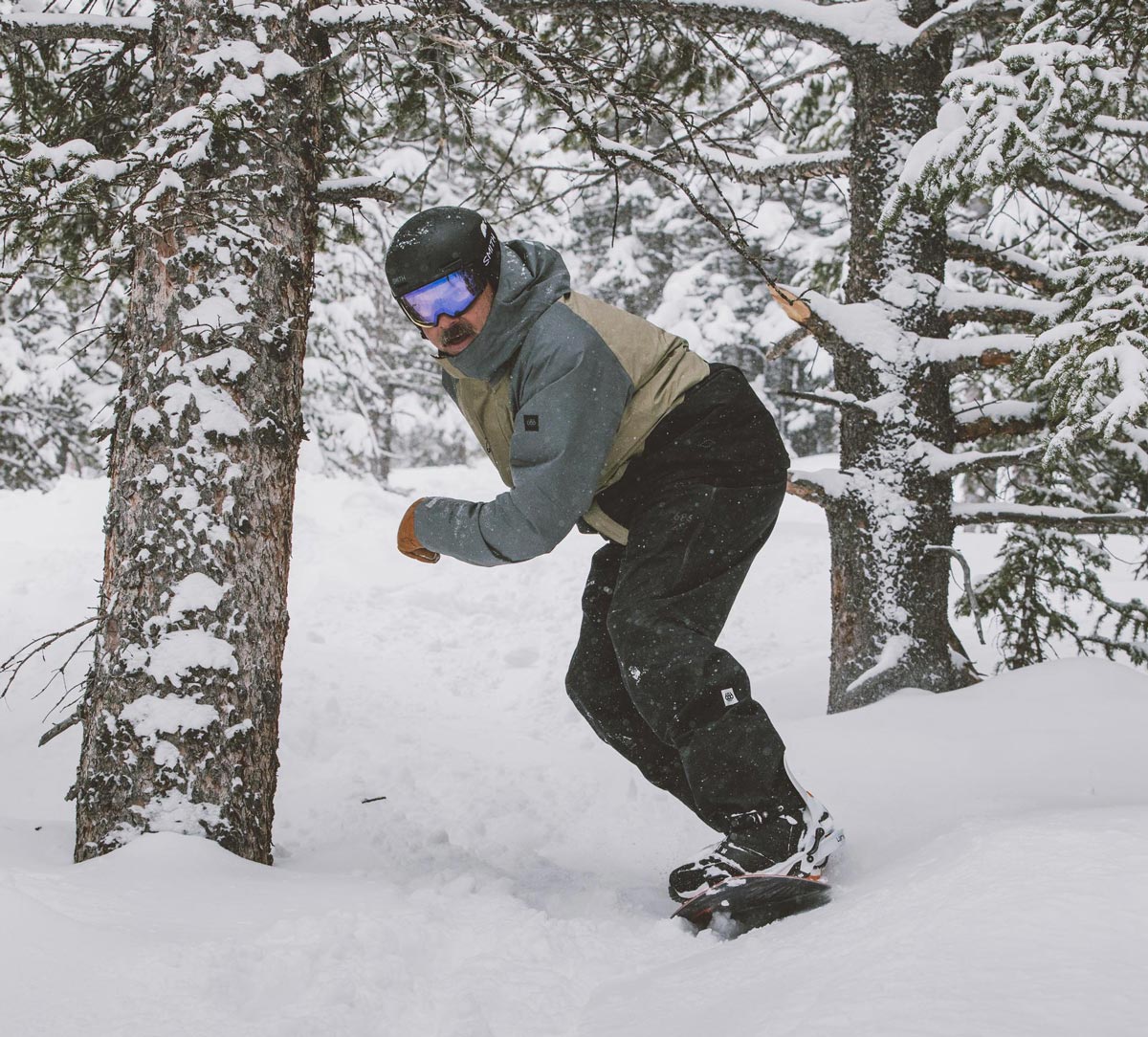 Male snowboarder riding on fresh snow while passing through snow-covered trees