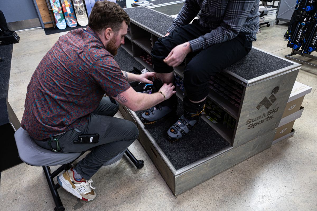 A Sun & Ski Sports Outdoor Expert Helping with snowboard boot fittings.