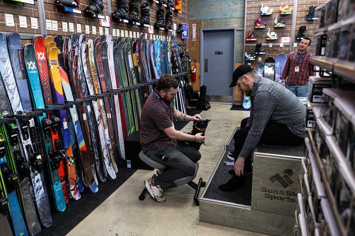 Outdoor Expert at Sun & Ski Sports fitting a male customer for ski boots in store