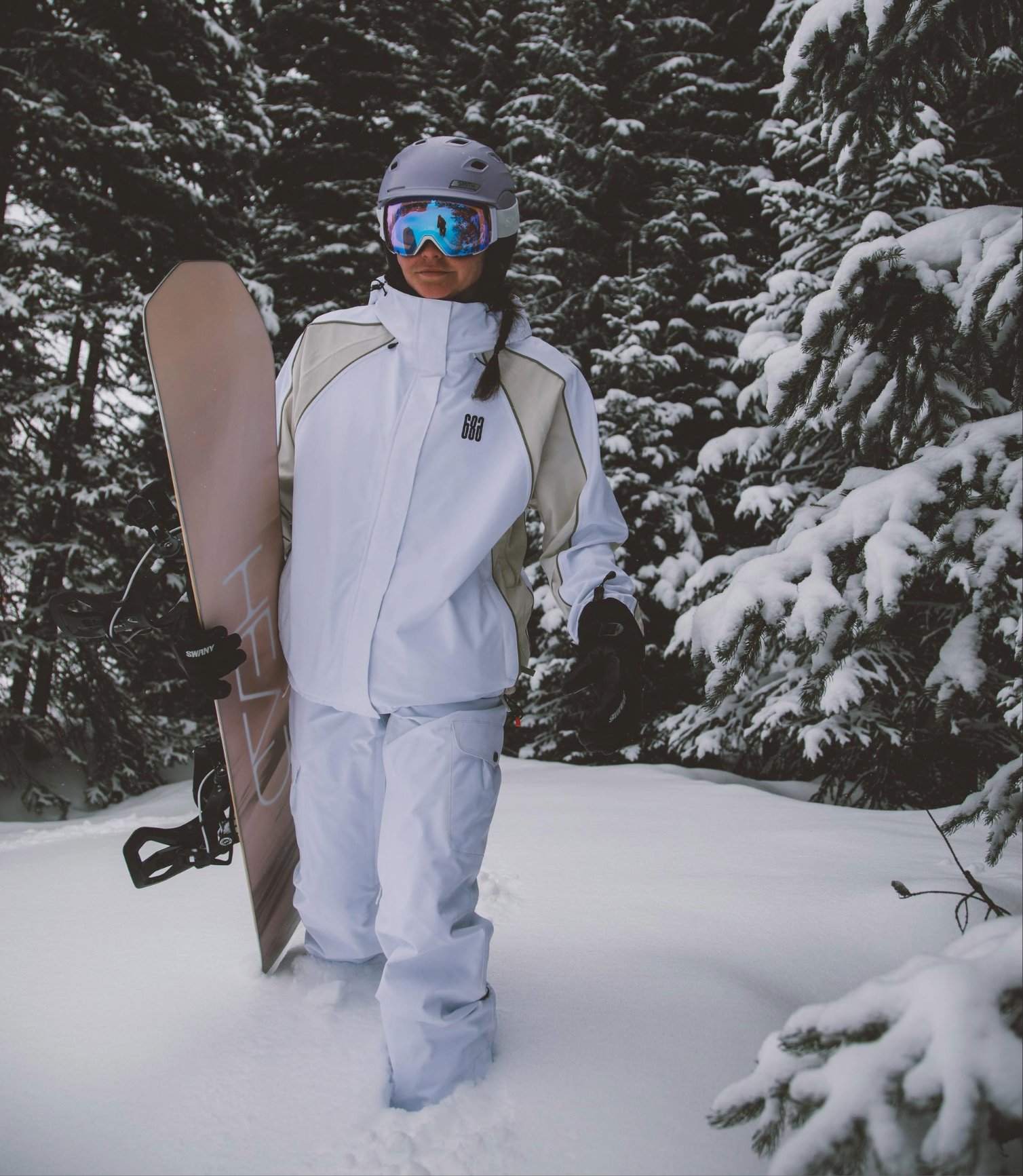 Snowboarder wearing a helmet and goggles, walking through fresh powder with a snowboard