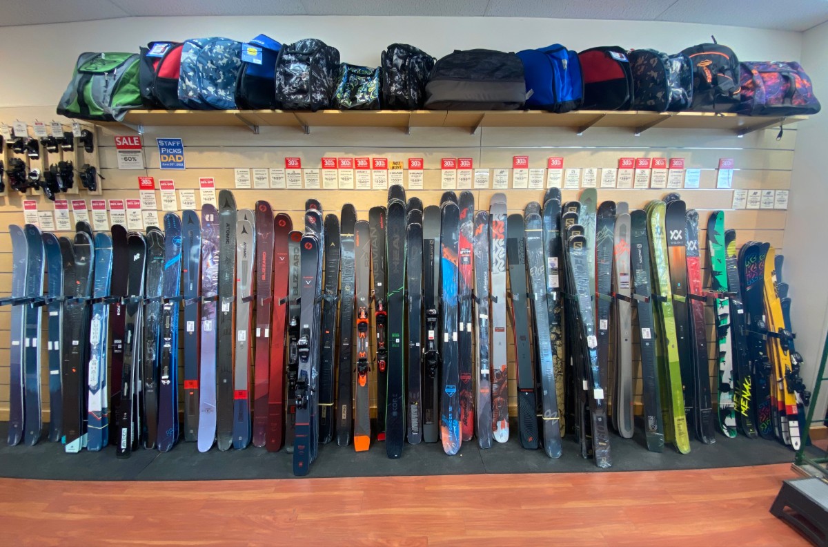 Wall display of skis in various colors at a Sun & Ski Sports location with sale price tags and equipment storage above.