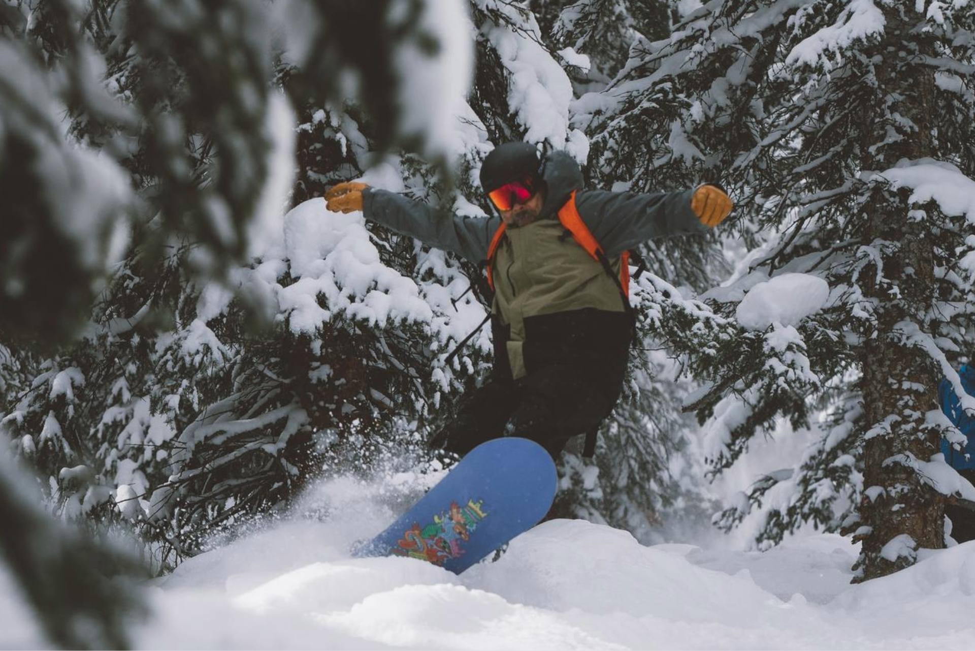 Snowboarder riding through deep powder in a snowy forest