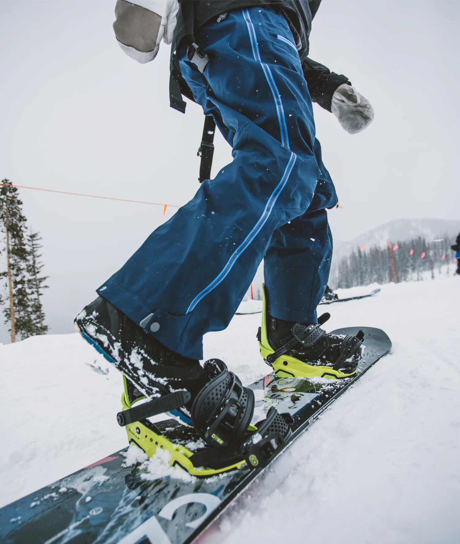 Snowboarder wearing insulated snow pants and boots, strapped into snowboard bindings on a snowy slope.