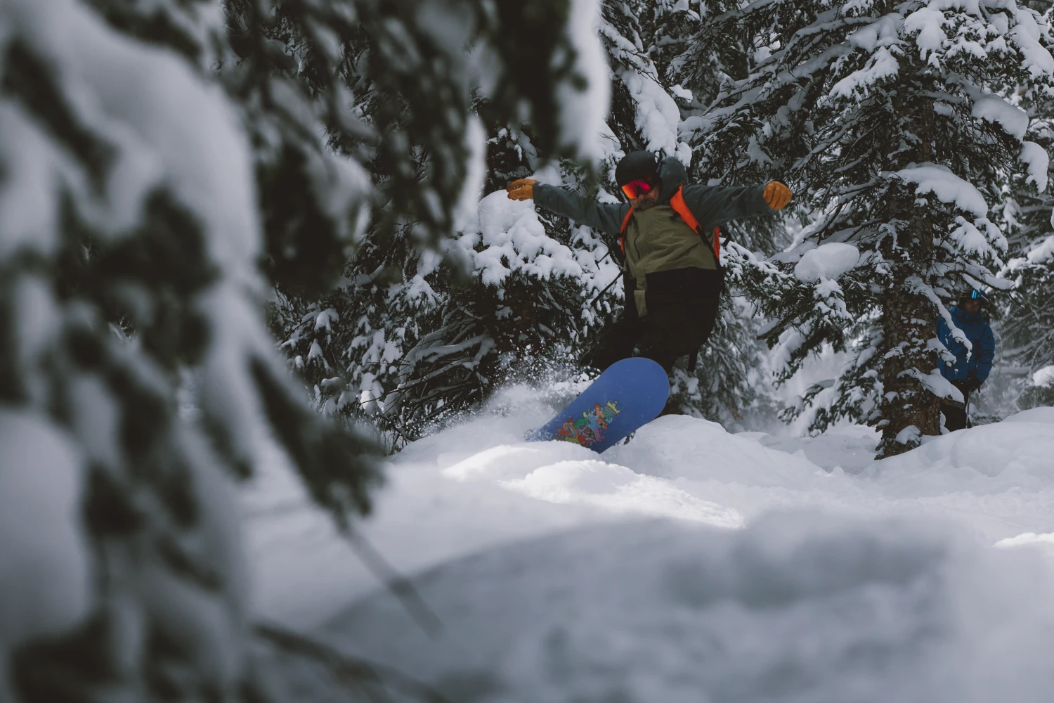Snowboarder riding through deep powder in a snowy forest.