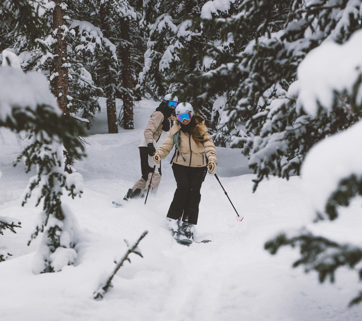 Woman skiing through pine trees, down a mountain of fresh powder snow