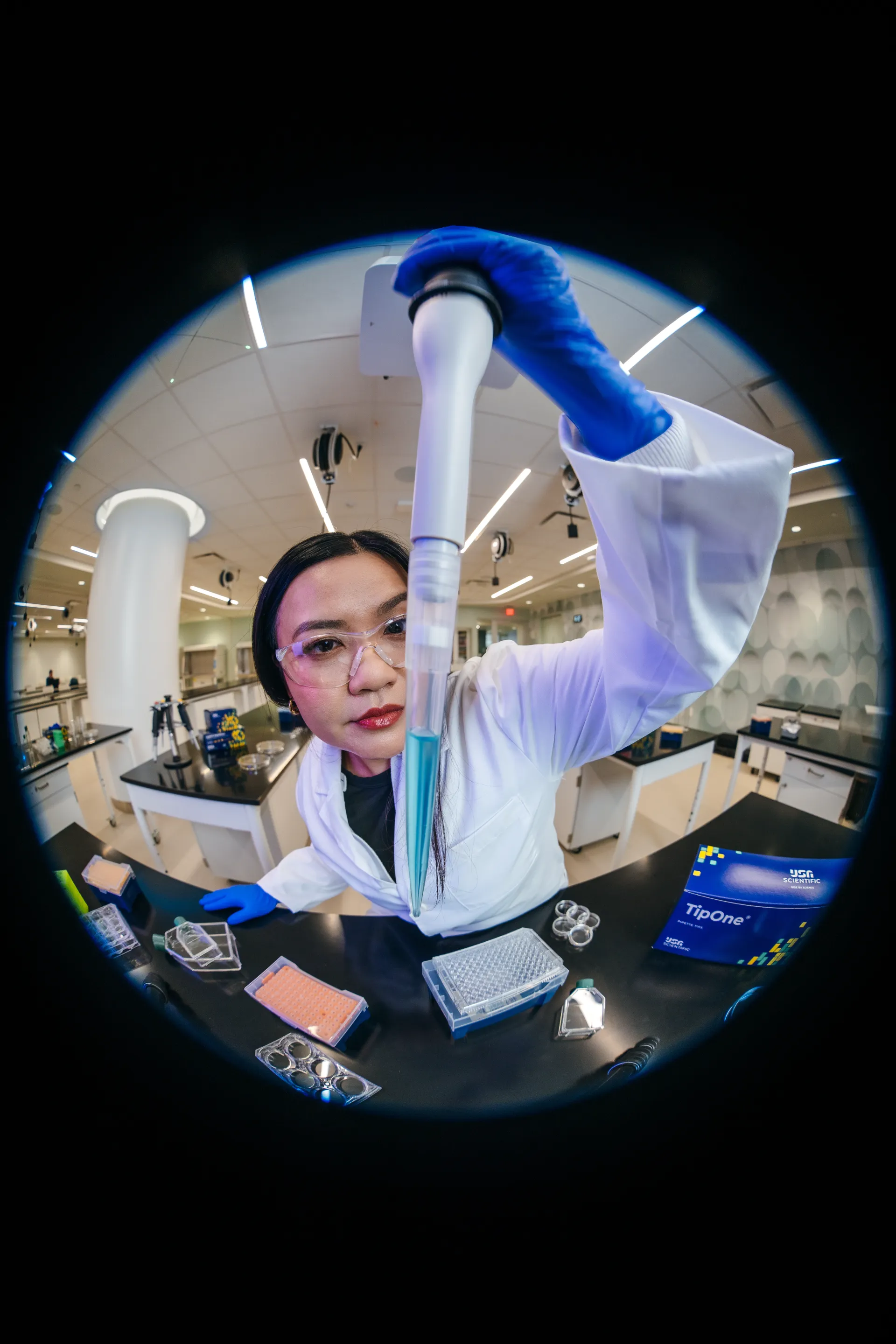 Scientist holding an electronic pipette under circular lens framing